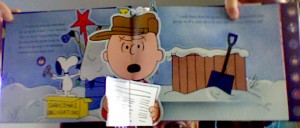 Pictue of a Pop-up page with Charlie Brown reading the contest announcement while Snoopy decorates his dog house